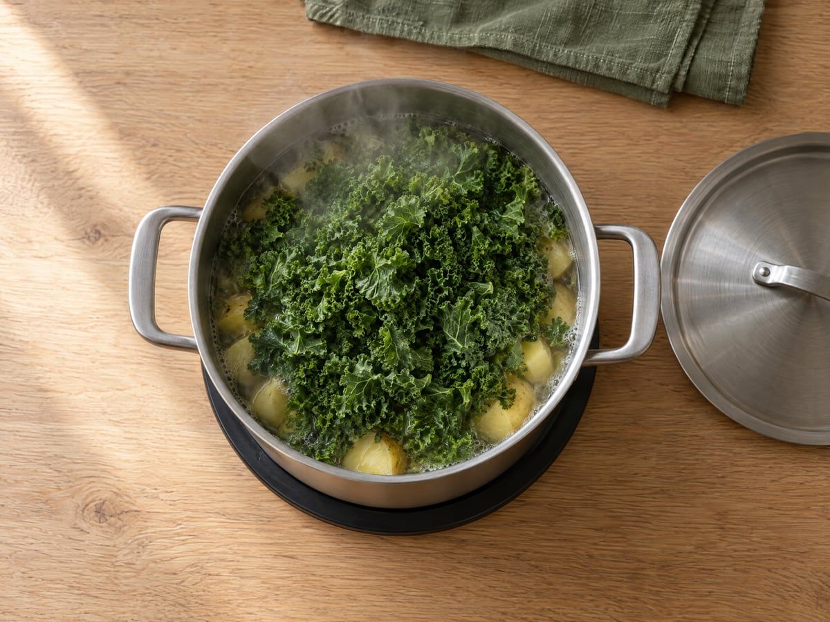 Pan met boerenkool bovenop de aardappelen, de deksel ernaast
